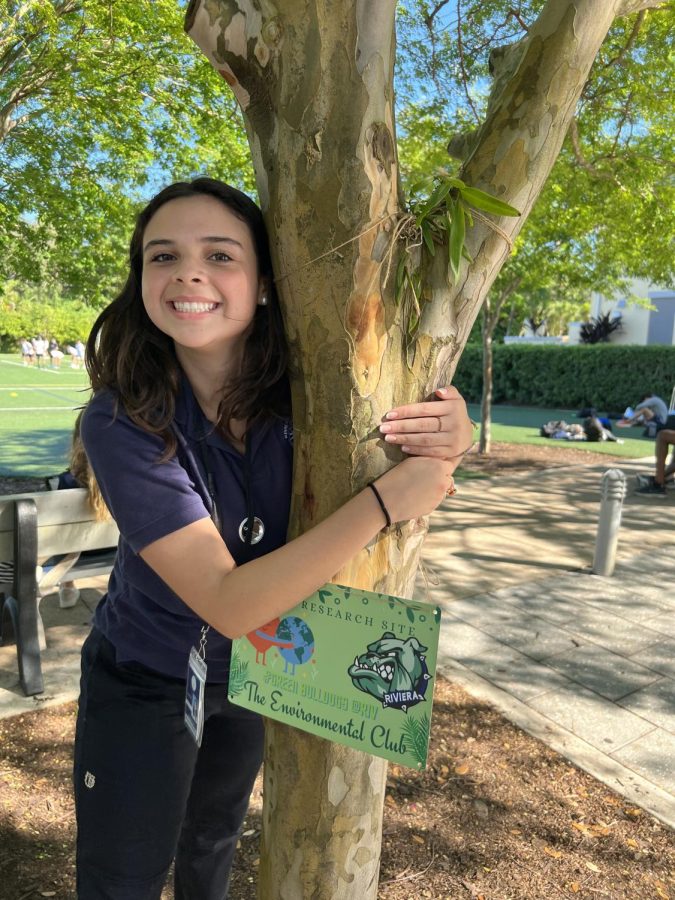 Alejandra Lopez (12) hugs a tree with the Environmental Club logo. (Yilena Sanchez)