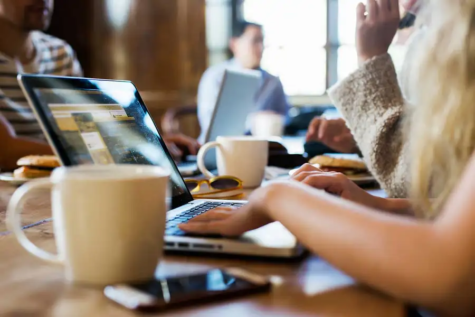 Stock image of coffee mugs and laptops on a table.