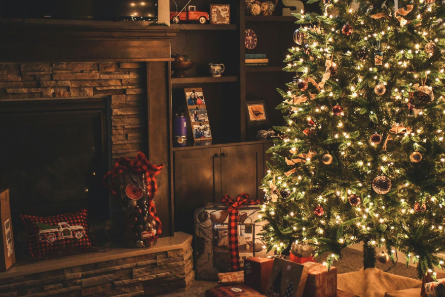 Gifts are stacked beneath a brightly decorated Christmas tree inside a cozy living room.